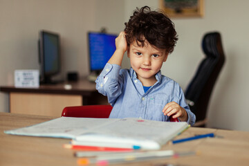 Preschool education online. A cheerful and energetic preschooler at the computer is engaged, next to notebooks, pencils. Lesson with a teacher remotely.