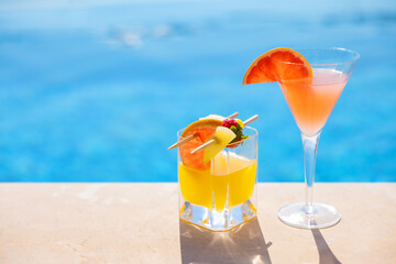 Two glasses of cocktails with fresh fruits by the pool