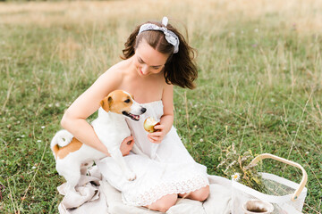 Caucasian beautiful girl on a summer day at a picnic. girl in a white dress and kerchief in a field. jack russell terrier dog playing with the owner. girl and dog playing. man and animal together. A l
