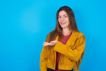 young brunette woman wearing yellow fringed jacket over blue background says: wow how exciting it...