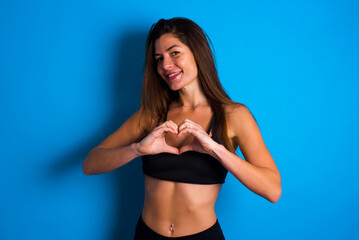Fototapeta na wymiar Young beautiful sportswoman doing sport wearing sportswear over blue background smiling in love showing heart symbol and shape with hands. Romantic concept.