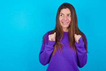 oung beautiful caucasian woman wearing purple sweater against blue background clenches fists and...