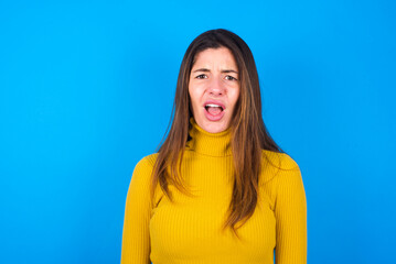 young beautiful caucasian woman wearing yellow turtleneck sweater against blue background yawns with opened mouth stands. Daily morning routine