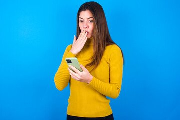 young beautiful caucasian woman wearing yellow turtleneck sweater against blue background being...