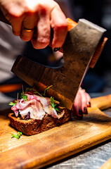 Woman chef hand cutting tasty sandwich with axe on wooden plate in kitchen