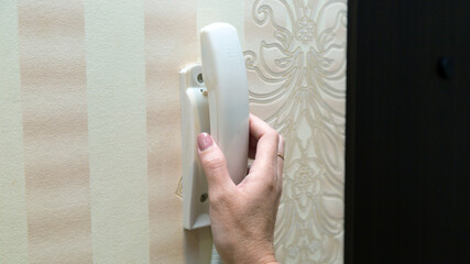 A woman hand lifts  white handle from the intercom inside apartment.
