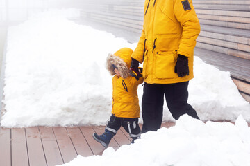Father and son in warm yellow jacket back, outdoor family time, man holding hands with his child. Snowy winter day