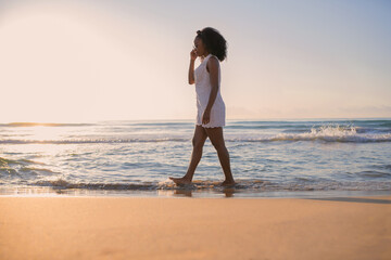 African american woman walking along the beach at sunset