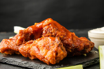 Traditional fried buffalo chicken wings in sauce close-up, dark background.