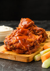 Delicious classic buffalo chicken wings drizzled with sauce and served on a wooden board.