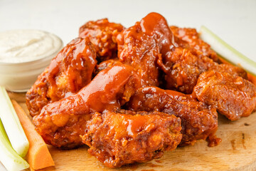 Fried buffalo chicken wings served with chopped vegetables on a white table.