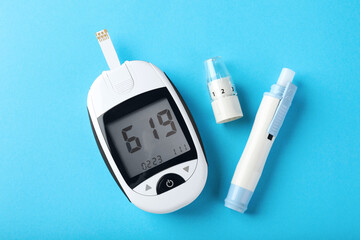 Digital glucometer and lancet pen on light blue background, flat lay. Diabetes control