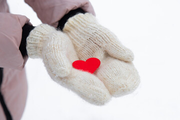 red heart lies on the fresh mittens. Winter snow. the woman dares in her palms a small red heart. close-up.