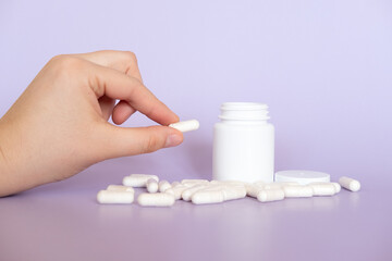 Hand and fingers holding medicine capsule in front of purple background