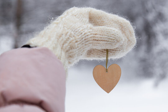 Woman holding wooden heart on winter snow background, close up. Valentines Day concept
