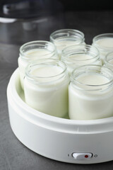 Obraz na płótnie Canvas Modern yogurt maker with full jars on grey table
