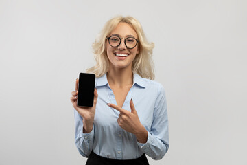 Fototapeta premium Business app. Happy business lady holding smartphone and pointing finger at blank screen, ligth grey studio background