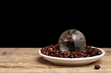 glass ball with world map in saucer with coffee beans on wooden table