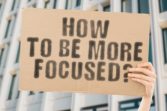 The question " How to be more focused? " on a banner in men's hand with blurred background. Intensive. Motivated. Professional. Opportunity. Individuality. Guidance. Determined. Determination