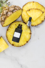 pineapple moisturizing serum in a black matte bottle lies on a juicy slice of fruit. Vertical top view. layout of an empty logotype.