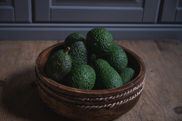 freshly harvested green avocados lie in a wooden bowl on a rustic wooden table
