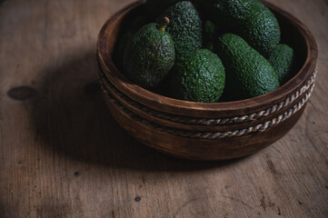 freshly harvested green avocados lie in a wooden bowl on a rustic wooden table