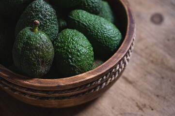 freshly harvested green avocados lie in a wooden bowl on a rustic wooden table