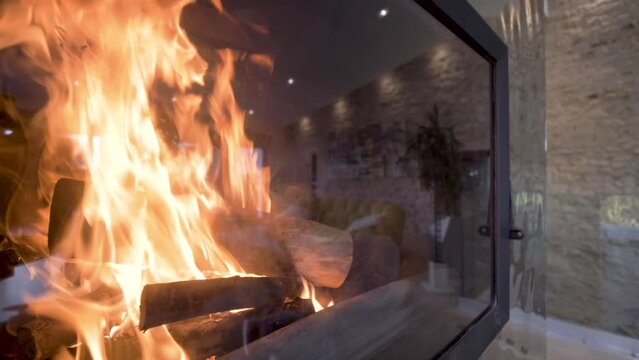 Luxury home fireplace with raging flames behind a glass case panel, Dolly out shot