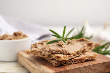 Crispy crackers with delicious meat pate and rosemary on wooden board, closeup