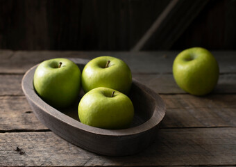 Still life with green apples on a platter on a wooden table.