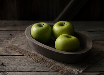 Still life with green apples on a platter on a wooden table.