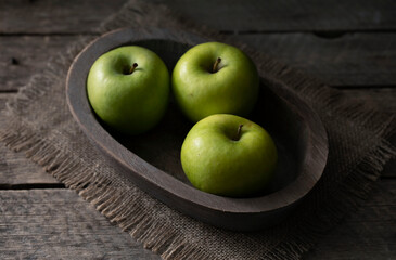 Still life with green apples on a platter on a wooden table.