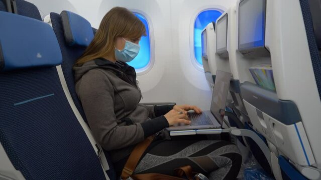 CLOSE UP: Productive woman on a long international flight is working on her laptop. Young female traveller works on her laptop during a long flight. Digital nomad working on computer while flying.