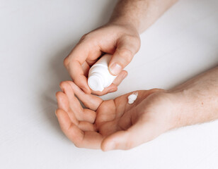 A man using moisturizing cream.Perfect groomed man hands holding white bottle and using moisturizing cream on white background. Care about clean, soft and smooth body skin. Closeup.