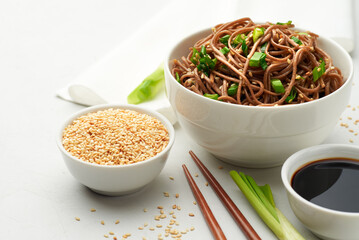 Oriental cuisine. Japanese soba with soy sauce, sesame, scallions on a white table with napkin and chopsticks . Horizontal photo with place for Your text.