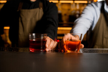 Two bartenders holding two glasses witg red and brown alcohol drinks