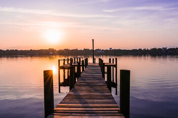 Obraz premium Pink sunrise with reflection in the river over the Sebastian River over a wooden pier in Little Hollywood, Mikko, Florida. Typical view of the beautiful nature in Florida