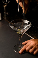 Hand holding tweezers and putting an olive into martini glass