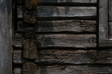 The surface of an old wall made of logs of a rural house. Logs blackened from time. Natural background. Old wooden house in the countryside. Brown rustic wood texture background.