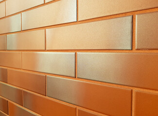 Modern facade made of orange ceramic tiles. New wall tiled bright orange bricks with a silvery gray shade, shining in the sun. Horizontal perspective receding into the distance. Background copy space.