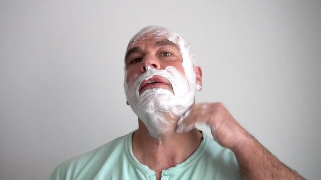 Close up of Caucasian man spreading shaving cream on his face and head to shave