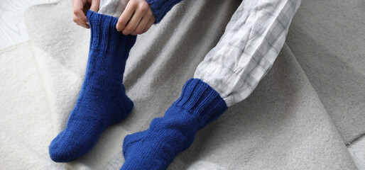 Woman putting on her warm knitted socks at home. Concept of heating season