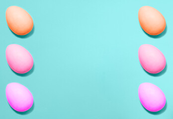 Naklejka na ściany i meble Easter holiday concept. Eggs colored with violet, pink and coral colors from sides on a blue background. Flat lay. Copy space for text, mock up. Banner.