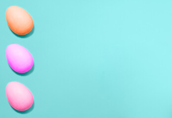 Three Easter eggs colored with violet, pink and coral colors from left side on a blue background. Flat lay. Copy space for text, mock up. Banner.