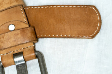 Beige belt made of thick genuine leather on a white background made of linen fabric. Production of handmade belts from natural environmentally friendly materials.