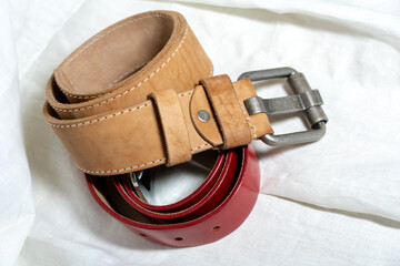 Two belts made of thick genuine leather on a white background made of linen fabric. Production of...