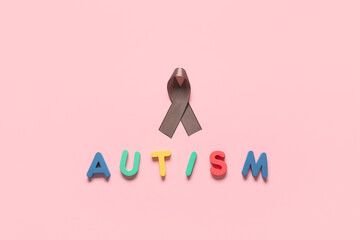 Word AUTISM with awareness ribbon on pink background