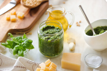Jar of pesto sauce and ingredients on light background