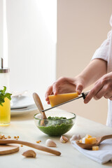 Woman grating cheese in pesto sauce on table in kitchen