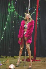 Beautiful young woman posing while dancing on pylon. Pole dancer in new year’s outfit. Celebration New Year, girl's party.
